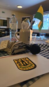 Tischszene beim Krombacher FanTalk: Mikrofon, Eintracht-Hagen-Unterlagen, Fanshop-Artikel und Fahne im Bayerischen Wirtshaus Humpert.